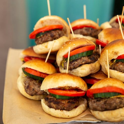 A tempting platter of mini burgers with fresh tomatoes and cucumbers, perfect for any gathering.